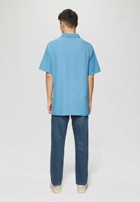 Kurzärmeliges, blaues Poloshirt aus weichem Material mit Kragen und lässiger Passform, kombiniert mit dunkelblauen Jeans und hellen Schuhen.