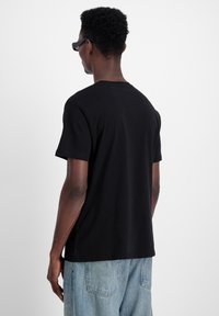 Schwarzes Baumwoll-T-Shirt mit lockerer Passform, Rundhalsausschnitt und kurzen Ärmeln, kombiniert mit hellblauen Jeans. Flache Rückansicht.