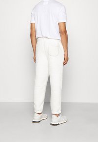 Vita fleecemjukisbyxor med bakficka, avsmalnande design och elastisk midja, kombinerade med en enfärgad vit t-shirt och vita sneakers.