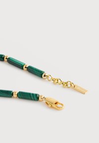 Κολιέ από πράσινο μαλαχίτη και χρυσά χάντρες με χρυσό κούμπωμα αστακού και ρυθμιζόμενη αλυσίδα σε λευκό φόντο.