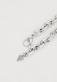 Collana in argento con maglie ovali, dotata di chiusura a gancio e di un'etichetta triangolare incisa con la scritta "GUESS." Texture liscia e lucida.