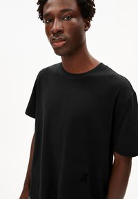 Schwarzes T-Shirt mit kurzen Ärmeln aus Baumwolle, mit Rundhalsausschnitt und einem dezenten Logo-Detail auf der unteren linken Vorderseite.