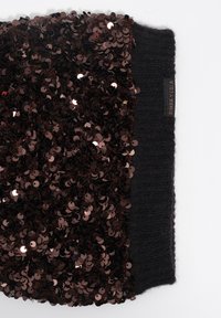 Accesorio de punto negro con parte superior adornada con lentejuelas circulares de bronce. Etiqueta visible: "Bimbay Lola." Tela texturizada que contrasta con los detalles brillantes.