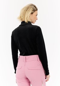 Zwarte ribbelige top met lange mouwen en hoge kraag, gecombineerd met roze broek met een gladde structuur en ritszakken.