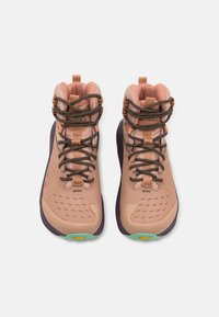 Rosa tursko med teksturert overdel, brune lisser og fleksible gummisåler. Har en fremtredende logo og Vibram-detaljer.