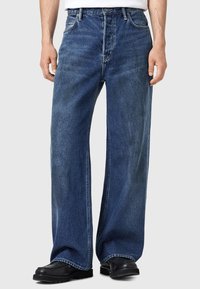 Siniset leveälahkeiset farkut, jotka on valmistettu puuvillasta ja joissa on haalistunut viimeistely, perinteinen viisi taskua -muotoilu ja näkyvät ompeluakkcentit.