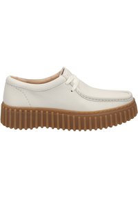 Scarpa in pelle bianca con punta rotonda e cuciture laterali, poggiata su una suola spessa e rigata di colore marrone, con profilo basso e lacci.