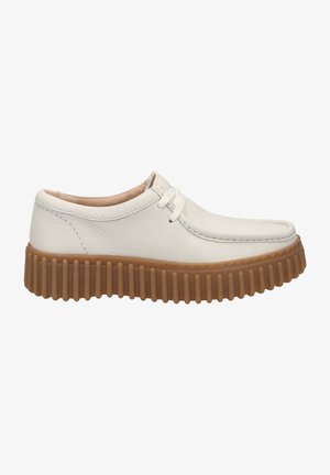 Scarpa in pelle bianca con punta rotonda e cuciture laterali, poggiata su una suola spessa e rigata di colore marrone, con profilo basso e lacci.