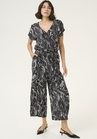 Black and white, abstract-patterned jumpsuit with short sleeves, V-neckline, elastic waistband, cropped wide legs, worn with black heels.