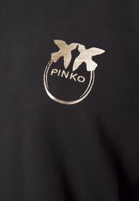 Tessuto nero con un logo metallico dorato che presenta due uccelli stilizzati e il testo "PINKO". Texture liscia con una leggera lucentezza.