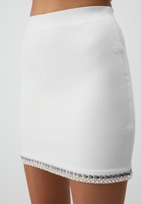 Witte mini-jurk van textuurstof, met een decoratieve zoom van zilveren kralen en heldere rechthoekige accenten. Glad, aansluitend ontwerp.