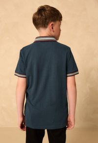 Mörkblå pik�étröja med en randig krage i vinrött, vitt och grönt. Kortärmad, slät textur och lätt figursydd design.