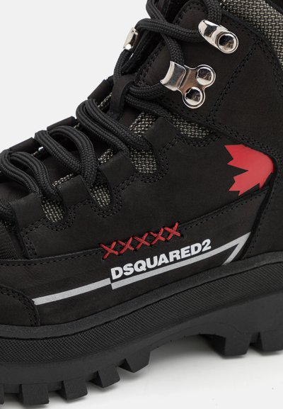 Czarne buty trekkingowe wykonane z zamszu i materiałów tekstylnych, z elementami w kolorze srebrnym, czerwonym i białym oraz solidną, teksturowaną podeszwą. Widoczne logo.
