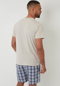 Camiseta de algodón de color beige claro con mangas cortas, combinada con pantalones cortos de cuadros azules y morados que presentan un patrón texturizado y un bolsillo lateral.