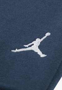 Ναυτικό μπλε ύφασμα με λεπτή υφή, που διαθέτει κεντημένο λευκό λογότυπο Jumpman στο πλάι, παρουσιάζοντας αθλητική σήμανση.