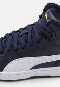 Sneakers alti navy con strisce laterali bianche, pelle testurizzata e fodera interna pelosa. Presentano lacci spessi e accenti di marca.
