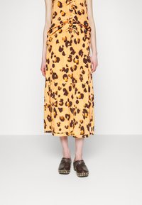 Robe imprimée léopard avec un détail froncé à l'avant dans des tons orange et marron, associée à des sabots marron foncé ornés de clous en métal.