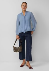 Hellblaue plissierte Bluse mit Schleifendetail, kombiniert mit dunkelblauen, weiten Jeanshosen. Dazu eine braune Schultertasche und burgunderrote Absatzschuhe.