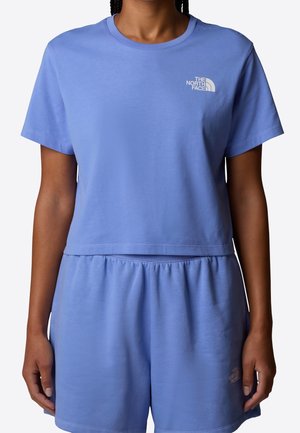 Osoba nosząca jasnofioletowy t-shirt z krótkim rękawem oraz pasujące elastyczne szorty z logo The North Face na piersi i lewym udzie.