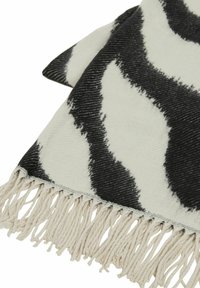 Musta-valkoinen kuvioitu peitto, jossa pehmeä pinta, hapsutetut reunat ja aaltoileva kuvio kankaan pinnalla.