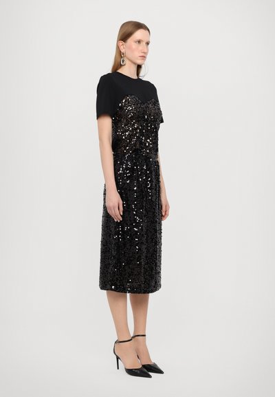 Mustaar kleit, millel on lühikesed varrukad, glitterist bodice ja istehoidev siluett, ulatudes kesk säärteni. Kombineeritud mustade kõrgete kontsadega.