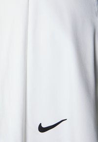 Tela atlética blanca con una textura suave, que presenta un logo negro de Nike cerca del hombro. El diseño es simple y funcional.