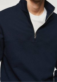 Sudadera de cuello redondo en azul marino con cremallera de un cuarto, que presenta una textura suave y un cuello de camiseta blanco en contraste debajo.
