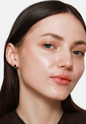 Orecchini a cerchio neri, finitura lucida, forma rotonda. Inquadratura ravvicinata di un viso con trucco leggero, pelle liscia e capelli castani.