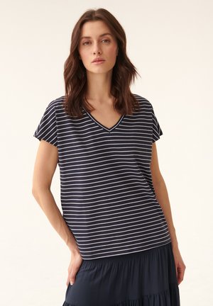 Námořnický v-neck tričko s bílými horizontálními pruhy, krátké rukávy, volný střih, spárováno s tmavou vrstvenou sukní, hladká textura.