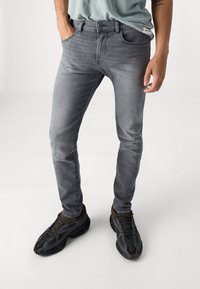 Grå denim jeans med slim fit, femficksdesign och kontrasterande sömmar. Parat med svarta träningsskor.