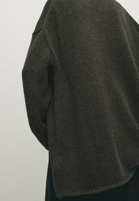 Tummanvihreä neulottu pusero, jossa on väljää mallia, teksturoitu kangas ja laskokaarrokkeet, leveällä ja rentouttavalla istuvuudella.