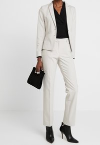 Vaalea beige bleiseri ja hyvin istuvat housut mustan paidanalla. Musta teksturoitu käsilaukku ja kyynärmittaiset kengät täydentävät asun.