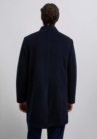 Abrigo de lana azul marino con una abertura en la espalda, gran cuello y mangas largas. La tela tiene una textura suave con detalles de costura mínimos.