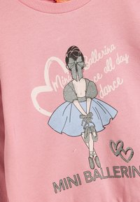 Rosa sweatshirt med en ballerina-grafik med silverdetaljer, texten "MINI BALLERINA" och hjärtformad design; mjukt bomullsmaterial.