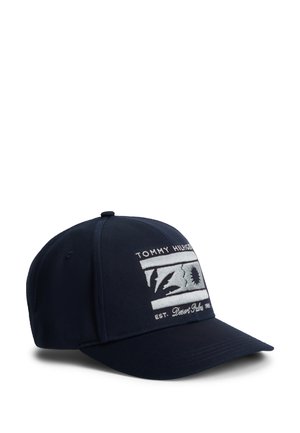 Șapcă baseball albastru marin cu o etichetă dreptunghiulară albă brodată, pe care este inscripționat „Tommy Hilfiger Desert Palm EST. 1985” și cu un design stilizat de soare și palmier.