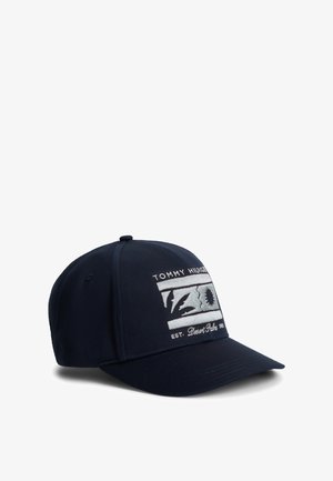 Marineblauwe baseballpet met geborduurde witte rechthoekige patch met de tekst "Tommy Hilfiger Desert Palm EST. 1985" en gestileerd zon- en palmboomontwerp.