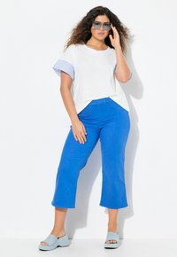 T-shirt bianco con maniche corte a righe blu, abbinato a pantaloni corti blu vivaci e sandali con zeppa azzurri.