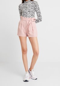 Haut à manches longues rayé noir et blanc associé à un short en lin rose taille haute, comprenant un nœud à l'avant et des détails plissés.