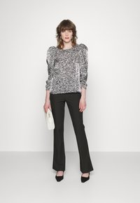 Blusa abstrata em preto e branco com padrões e mangas bufantes, combinada com calças pretas e uma clutch de cor creme. Sapatos de salto completam o look.