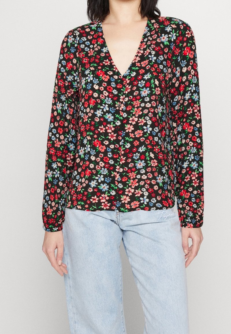 Blouse noire à fleurs avec un profond décolleté en V et des manches longues. Imprimée avec des fleurs rouges, bleues et vertes sur un tissu léger.