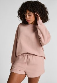 Lichtroze, zachte fleece sweatshirt met drop shoulders en ronde hals. Gecombineerd met bijpassende shorts met een elastische tailleband en een trekkoord.