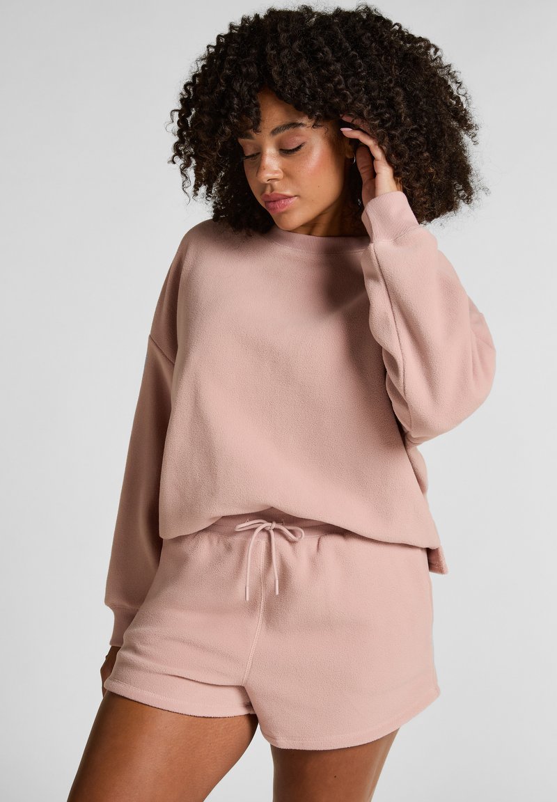 Lichtroze, zachte fleece sweatshirt met drop shoulders en ronde hals. Gecombineerd met bijpassende shorts met een elastische tailleband en een trekkoord.
