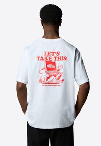 Bílý bavlněný tričko s červenou grafikou na zádech, na které je text a karikatura notebooku s rukama a nohama proti horskému pozadí.