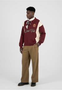 Maglione bordeaux e crema con colletto polo, dotato di logo ricamato e testo "Social Club". Abbinato a pantaloni marroni a gamba larga.