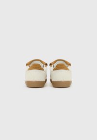 Back view of light-colored shoes with a textured design, featuring brown suede accents and a rubber sole.