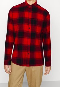 Rode en zwarte geruite flanellen shirt met lange mouwen, knoopsluiting aan de voorkant en puntige kraag; gemaakt van zachte stof met een gladde textuur.