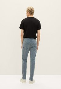 T-shirt noir à manches courtes, jean bleu clair et baskets blanches. Tissu lisse et coupe droite. Pas de motifs visibles ni de détails matériels.