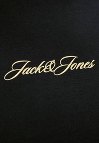 Tissu noir avec texte en cursive couleur crème indiquant "Jack & Jones", centré horizontalement.