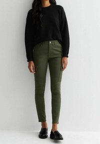 Jersey negro texturizado con cuello redondo, combinado con pantalones cargo ajustados en color verde oliva con bolsillos laterales, llevados con mocasines negros.