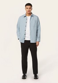 Lichtblauw, langmouwen shirt met knoopsluiting, een borstzak en donkere knopen, gecombineerd met zwarte broek en schoenen.